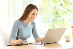 en kvinne som tegner på en tablet ved siden av en PC